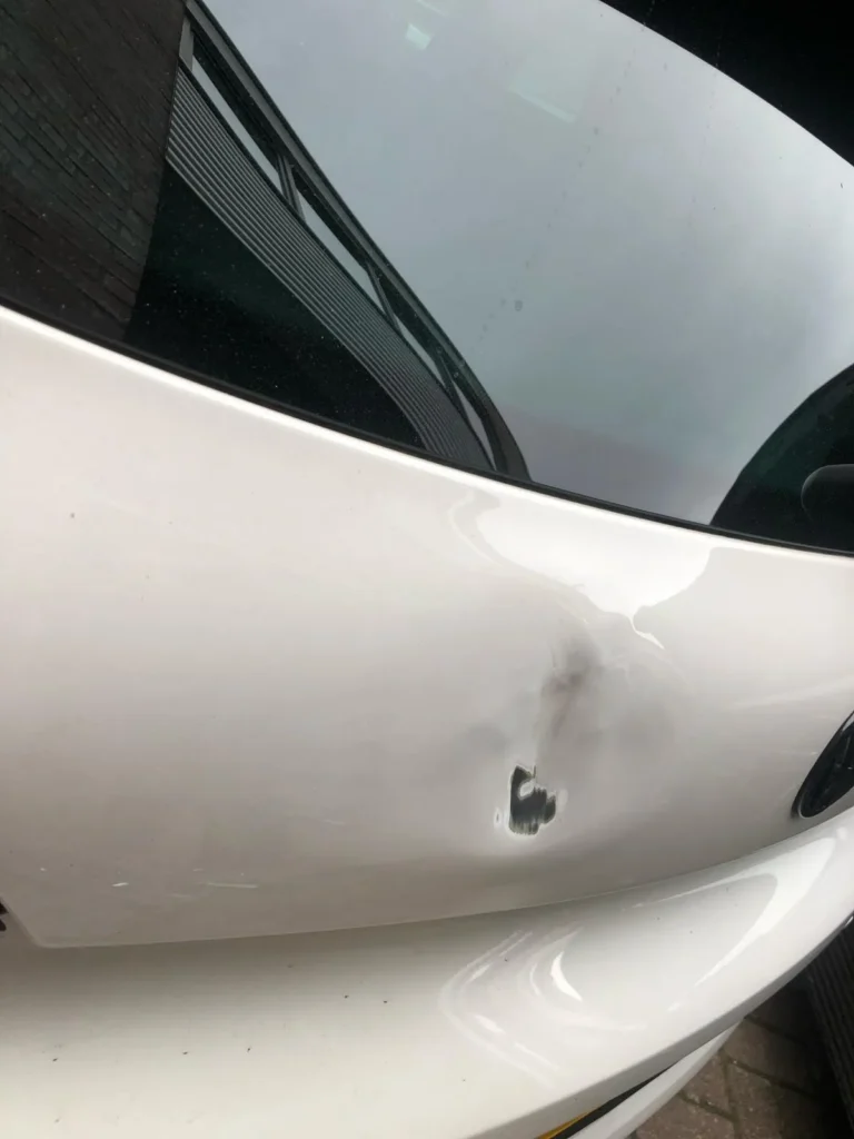 Witte hatchback met deuk bij het achterlicht
